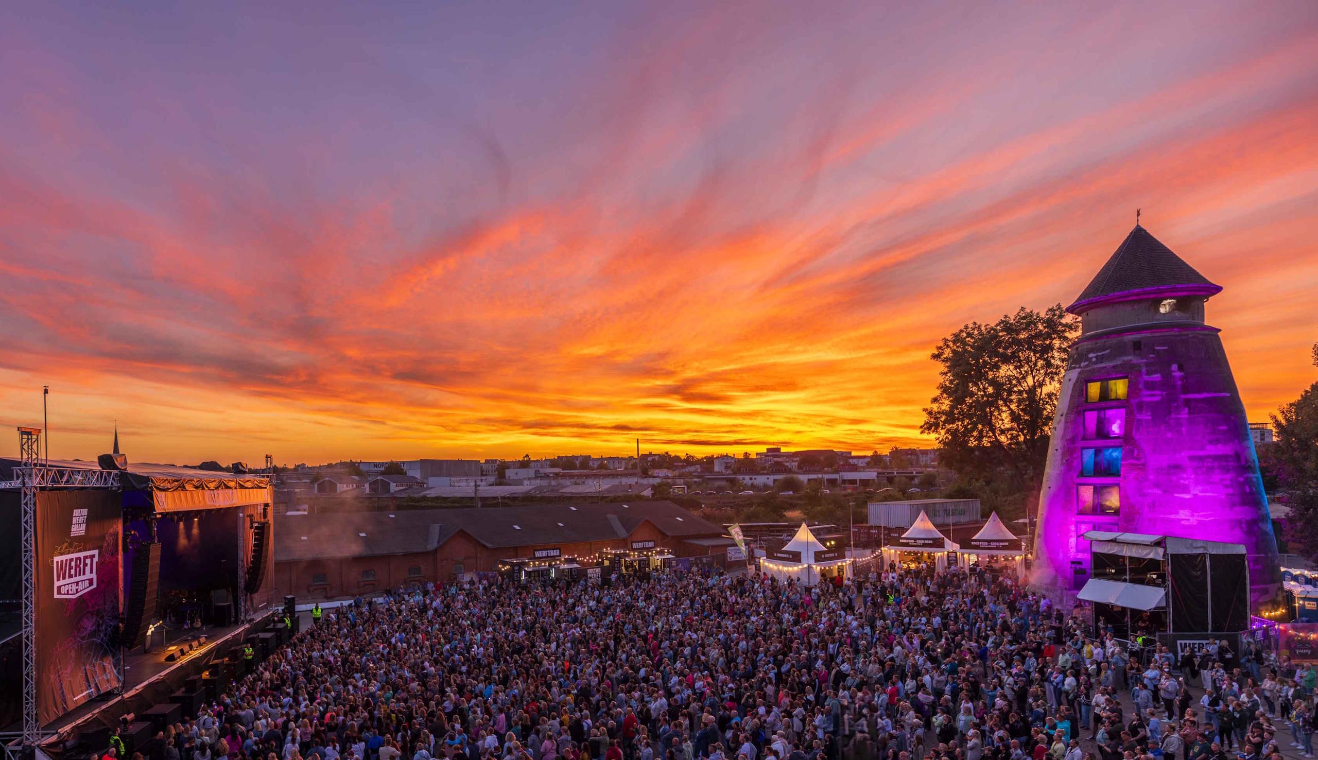 Werft Open Air im Lübecker Werftquartier bei Sonnenuntergang mit Bühne, Publikum und illuminiertem Wasserturm.